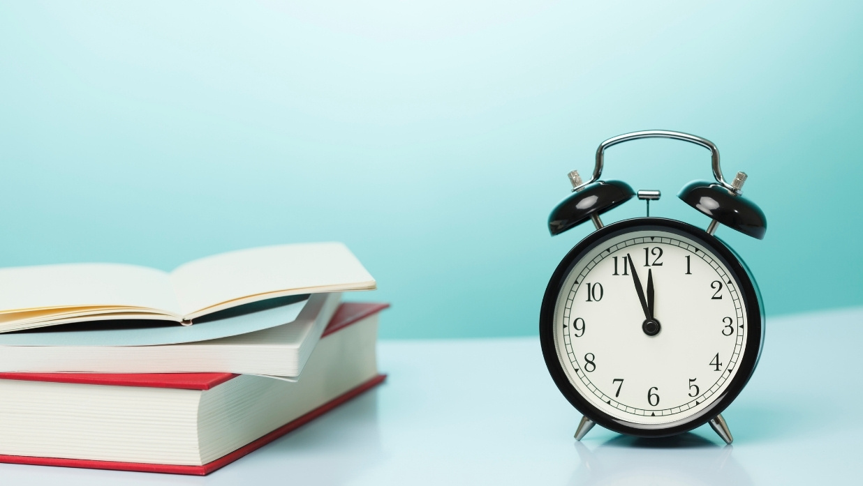 Classic black alarm clock next to study books, symbolizing the time and effort needed to prepare for the JLPT exam.