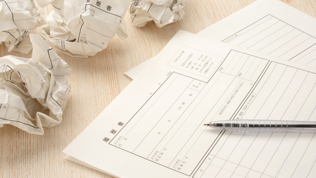 Des formulaires de CV japonais (履歴書) accompagnés d’un stylo sur un bureau, entourés de brouillons froissés — représentant le processus de rédaction d’une candidature au Japon.