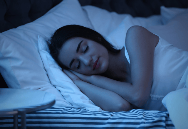 Une femme dort paisiblement dans un lit, éclairée par une lumière bleutée douce, symbolisant la tranquillité et la nuit.