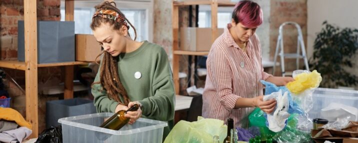 2 people sorting garbage to make sure everything is where it is supposed to be. Plastic bags, glass bottles, and more are on the table. Containers there for organization.