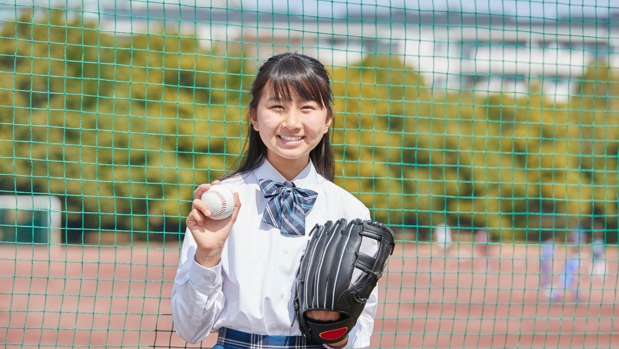 Girl holding a baseball and a mitt on a baseball field.