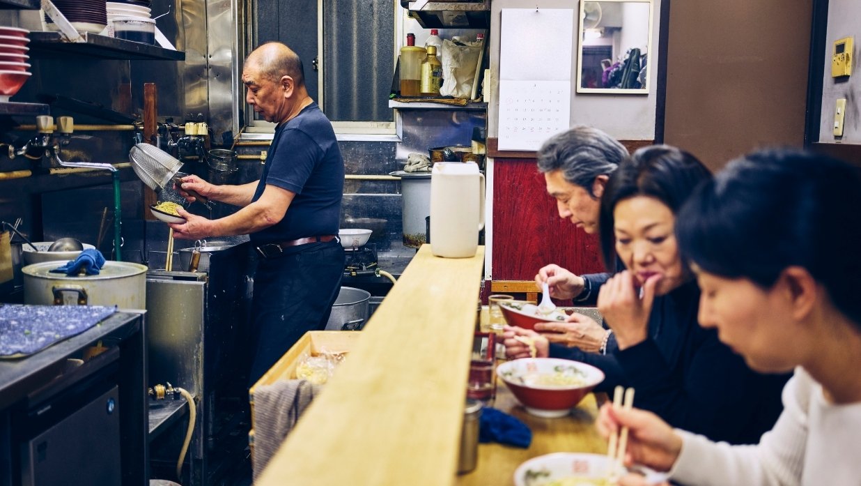 Ramen shop chef making food for guests. Guests already started eating.