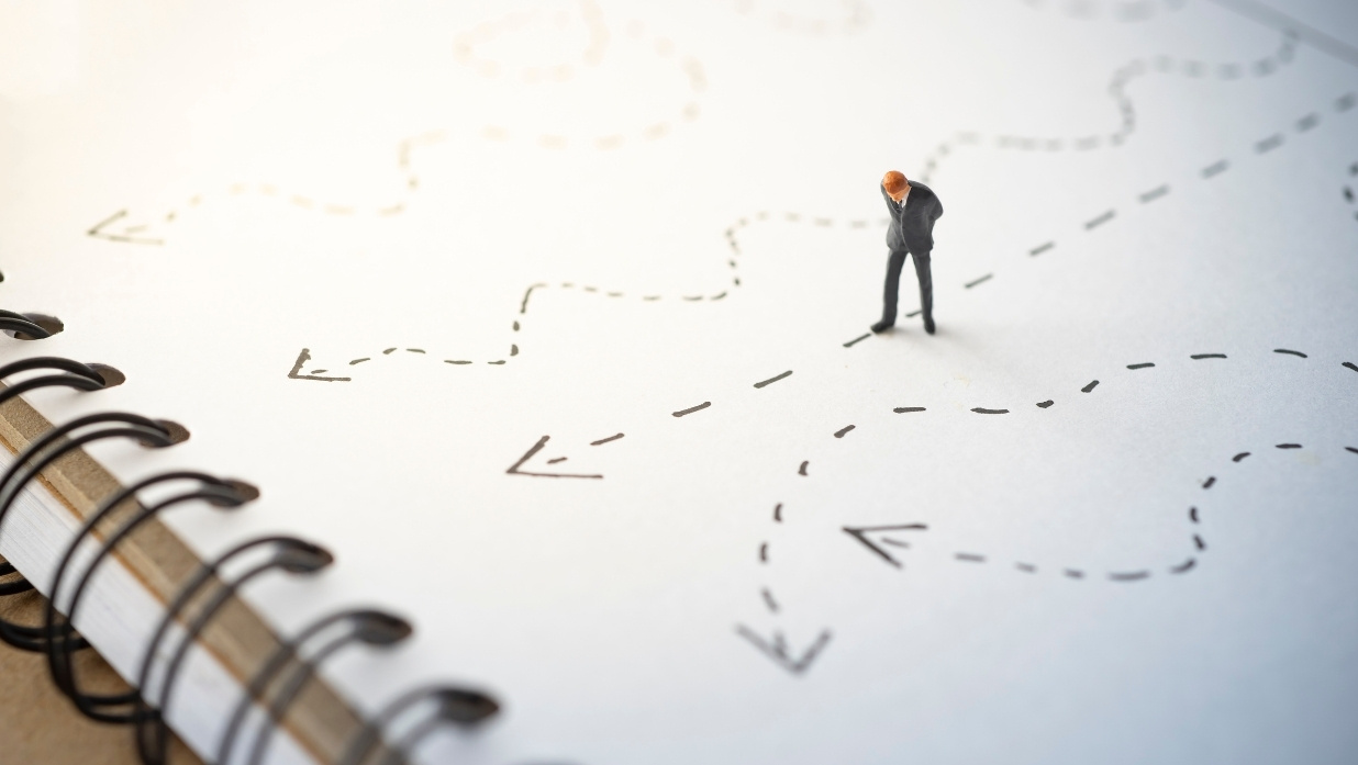 A figurine looking down at different drawn out directions on a paper.