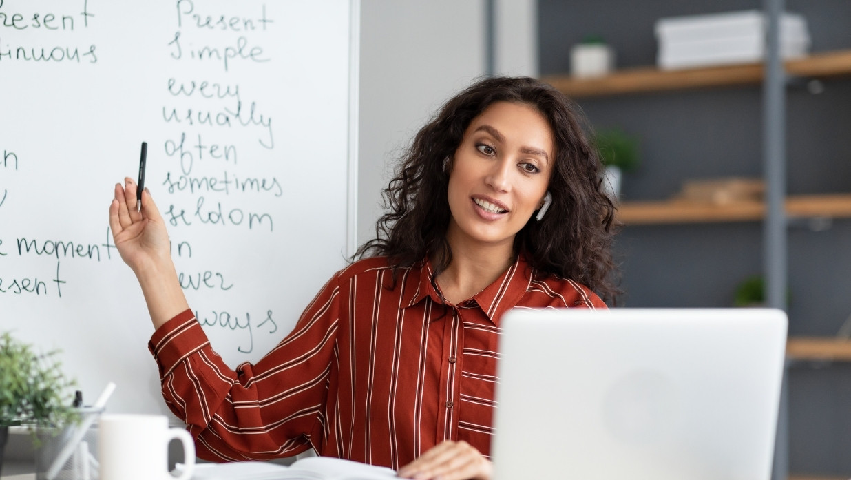 A woman practicing her grammar on a whiteboard from a computer screen.
