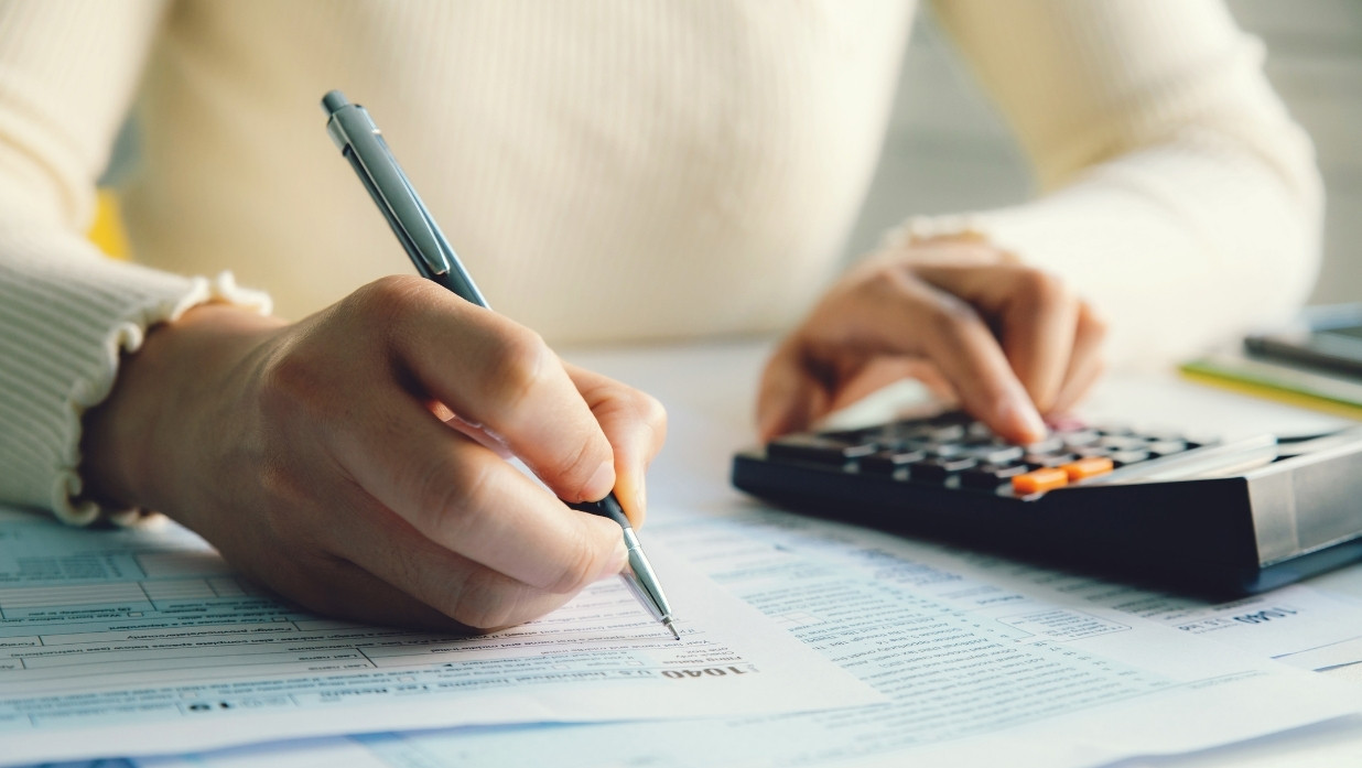 Persons hands showing as they do taxes on a worksheet and use a calculator