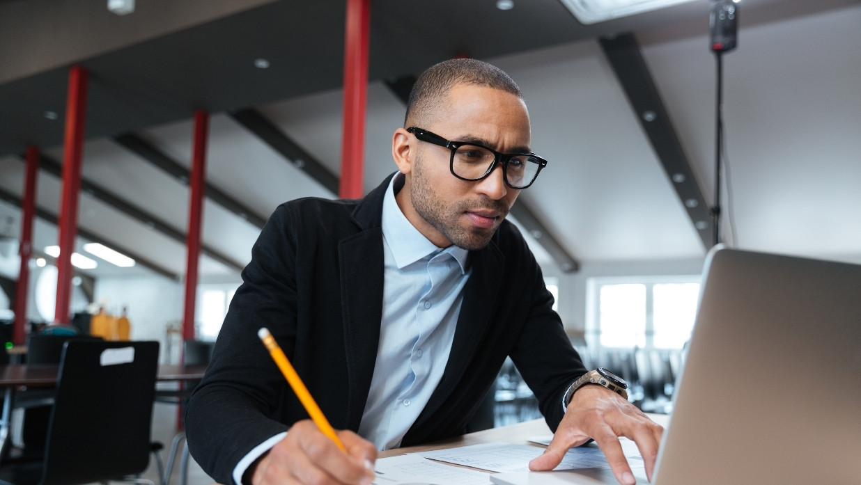 Man reading a computer screen and writing down what he is reading. Business casual wear.