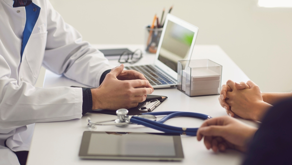 Doctor talking to a patient. Can only see their hands and the Dr's desk.