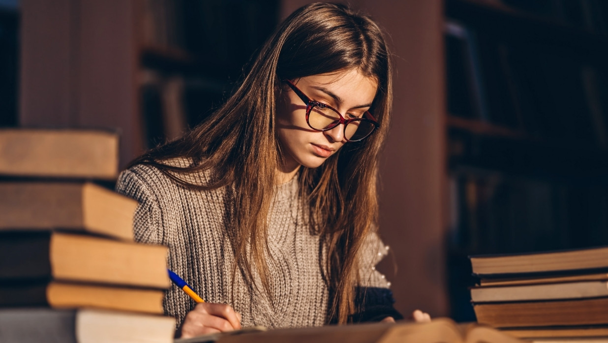 Girl studying for an exam. Glasses to help her focus. Books around her used for studying.