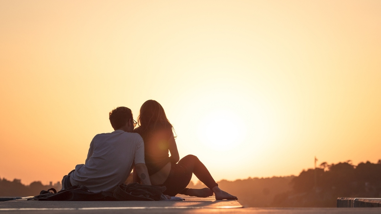 Dating in Japanese Tsukiau and Deeto - Picture of a man and woman sitting and looking at the sunset. Very close to each other on a date.